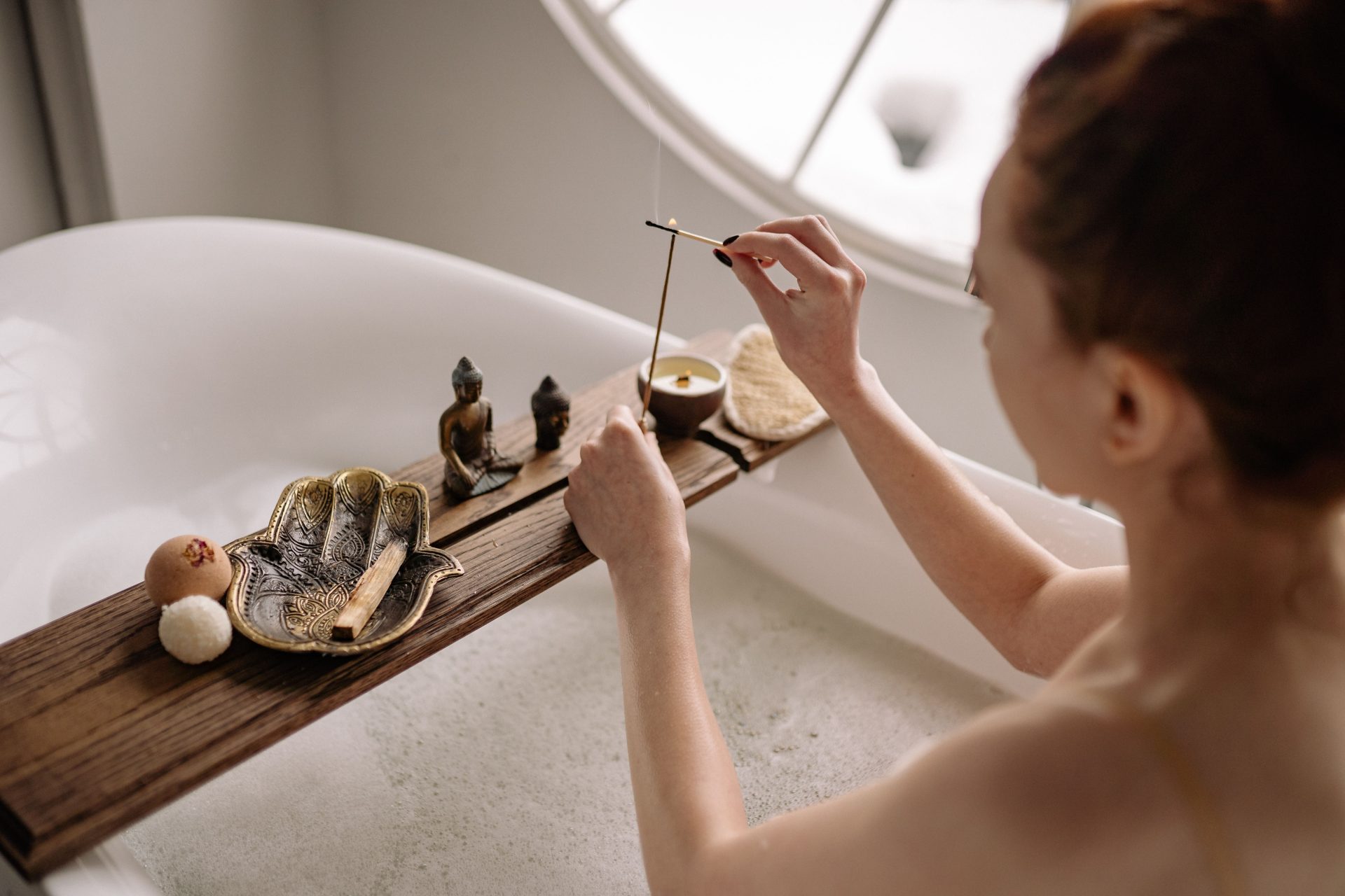 A woman enjoying a soothing bath ritual, lighting incense with decorative elements on a bathtub tray.